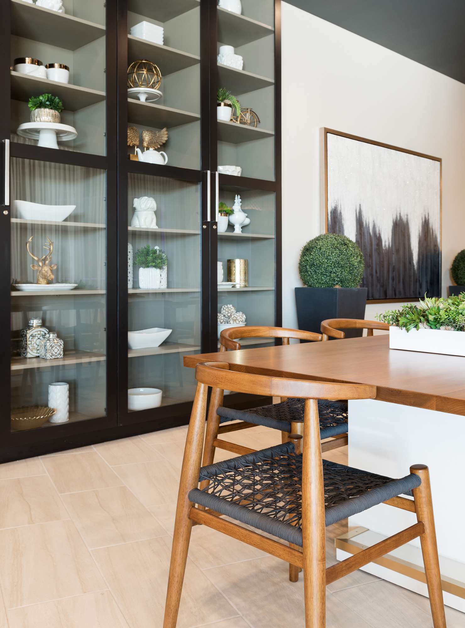 A clubroom is shown depicting modernist wood desk chairs and a china cabinet with a black finish and large glass doors. 
