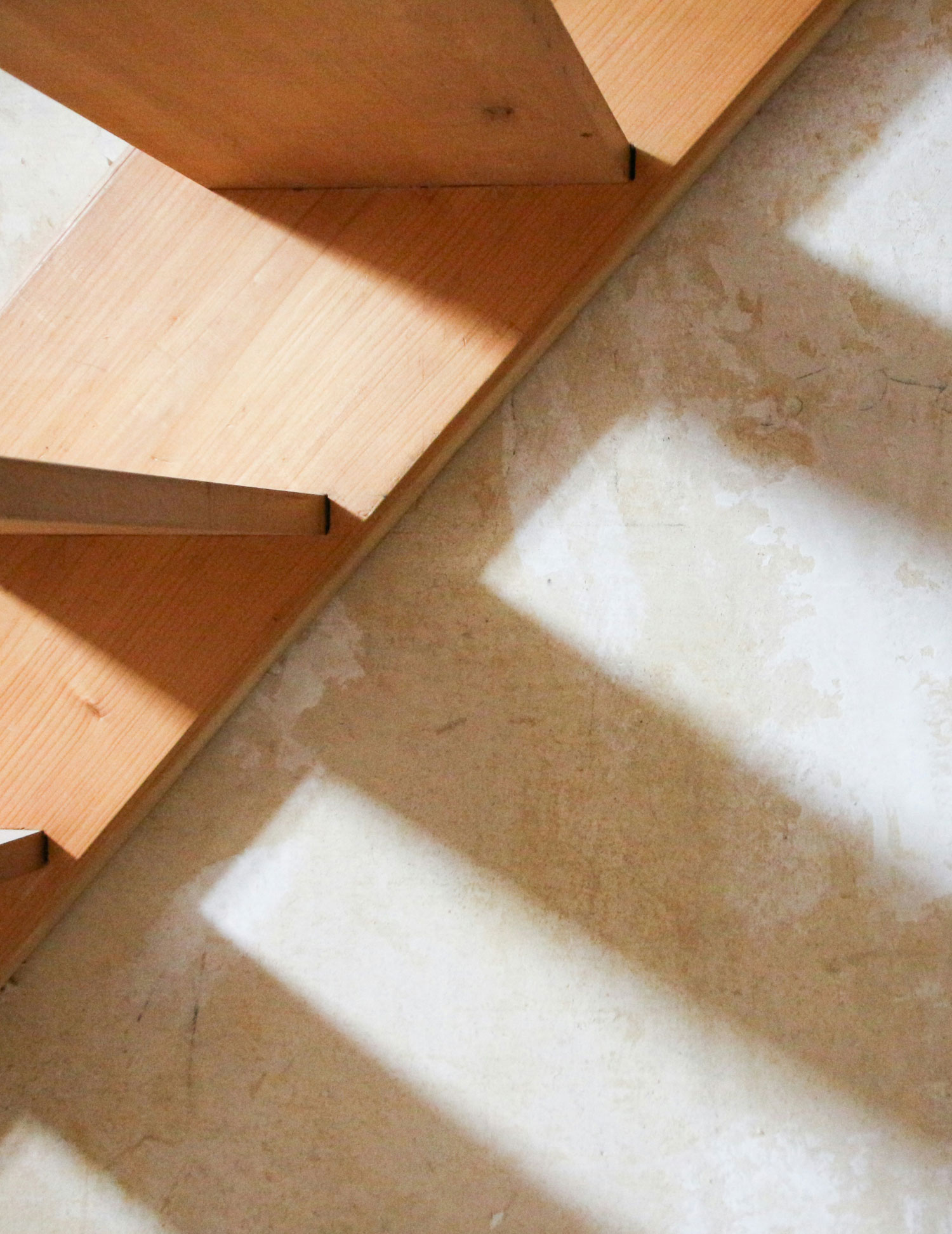A bed and metal nightstand are shown against a wall with brown concrete treatment. A white vase and candle sit atop a marble tray on the nightstand.