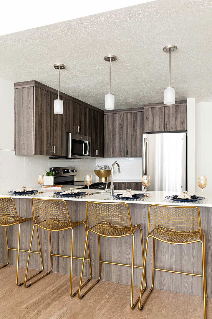 A modern kitchen with sleek stainless steel appliances. The bar is set up with place settings and wine glasses for four people. There are also four gold bar stools.